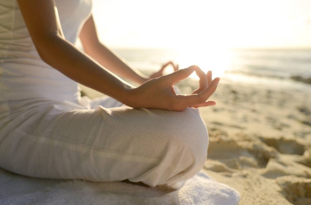 Women sitting on the beach practising yoga.